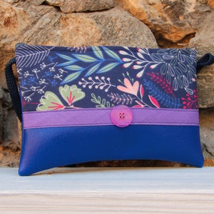 May include: A small blue and purple purse with a floral print and a single button closure. The purse has a short strap.