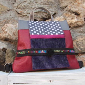 May include: A burgundy leather backpack with a grey, white and pink polka dot fabric panel, a blue denim fabric panel, and a black and colourful patterned strap.