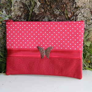 Peut inclure: Une pochette en tissu rouge à pois blancs avec un fond en cuir rouge et un accent papillon en métal. La pochette a une fermeture éclair.