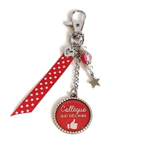 Op de afbeelding: Sleutelhanger met een rood lint met witte stippen en een zilveren hanger met de tekst "Collègue qui déchire" met een duim omhoog.