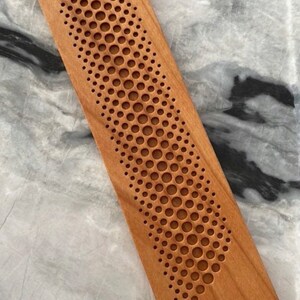 May include: A wooden rectangular block with a pattern of small circles carved into the surface. The circles are arranged in a curved line, creating a wave-like design.