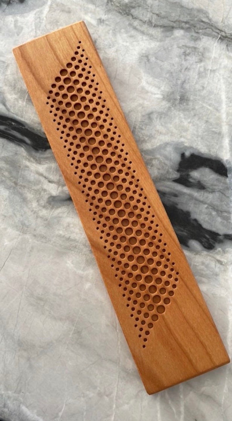 May include: A wooden rectangular block with a pattern of small circles carved into the surface. The circles are arranged in a curved line, creating a wave-like design.
