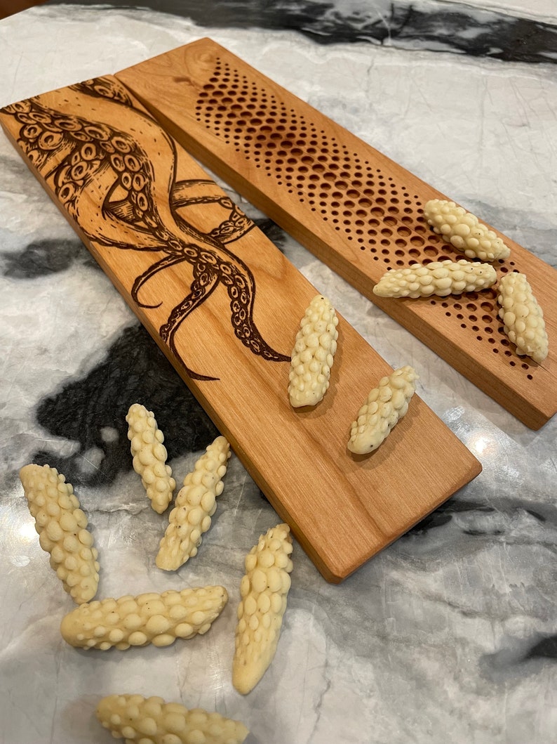 May include: Two wooden serving boards with a decorative design. One board features a detailed illustration of an octopus, while the other has a repeating pattern of circles.  The boards are surrounded by small, white, textured, food items.