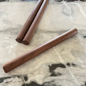 May include: Three wooden dowels, two are stacked on top of each other, and the third is lying horizontally on a white marble surface.