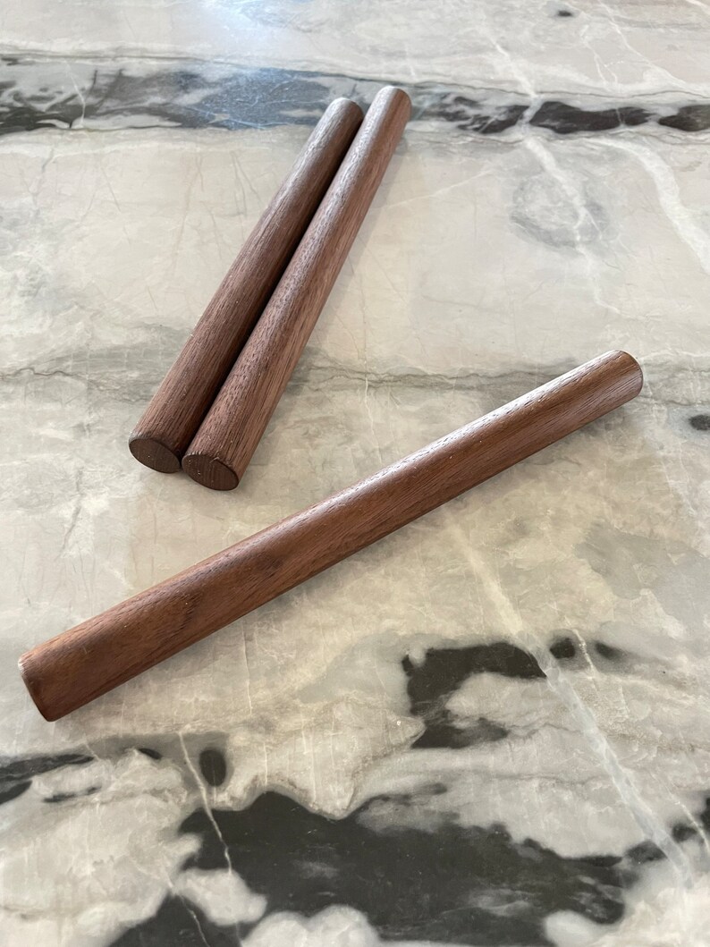 May include: Three wooden dowels, two are stacked on top of each other, and the third is lying horizontally on a white marble surface.