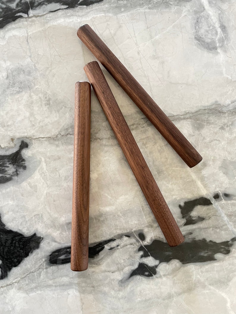 May include: Three wooden dowels, each about 12 inches long, are arranged in a triangular shape on a white marble surface.