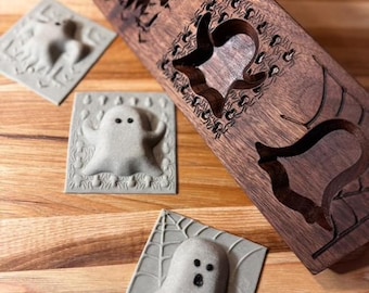 May include: Three gray ghost-shaped cookie cutters with a wooden cookie cutter with a ghost, spider web, and bat design. The wooden cookie cutter is made of walnut wood.