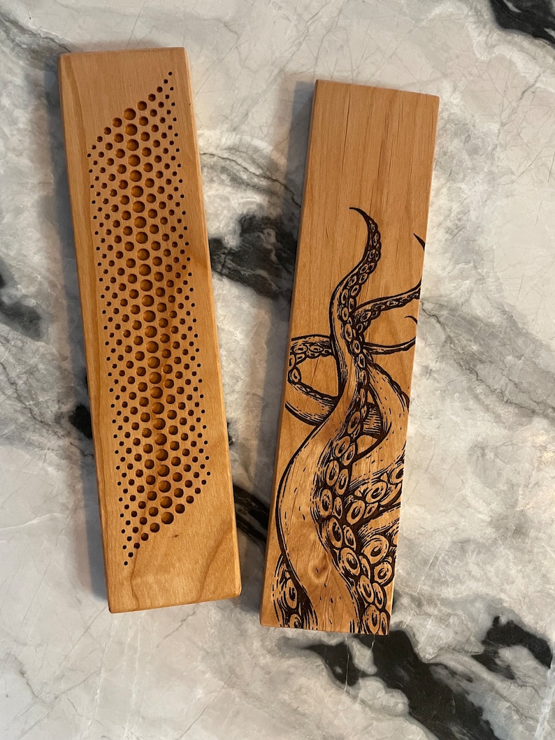 May include: Two wooden coasters with different designs. One coaster features a geometric pattern of circles, while the other has a detailed illustration of an octopus.