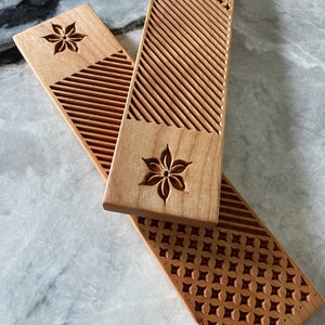 May include: Two wooden rolling pins with intricate carved designs. One pin features a geometric pattern and the other has a floral design.