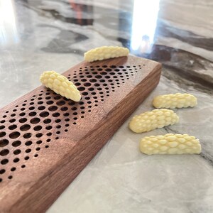 May include: Five white chocolate pieces shaped like a cluster of grapes, arranged on a light brown wooden surface with a patterned design.