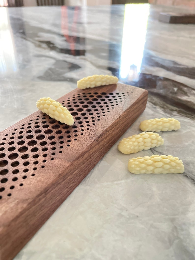 May include: Five white chocolate pieces shaped like a cluster of grapes, arranged on a light brown wooden surface with a patterned design.