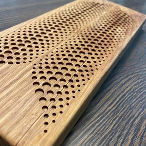 May include: A wooden cutting board with a unique design of a wave pattern made of small circles. The board is made of light brown wood and has a natural finish.