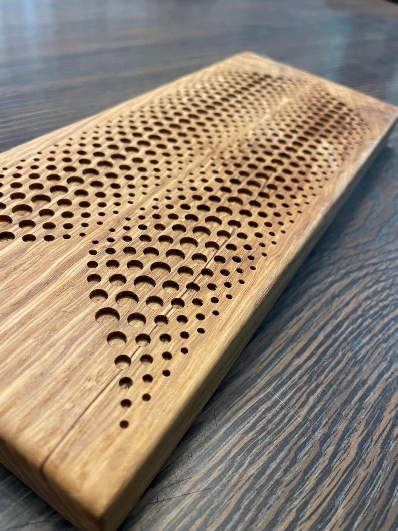 May include: A wooden cutting board with a unique design of a wave pattern made of small circles. The board is made of light brown wood and has a natural finish.