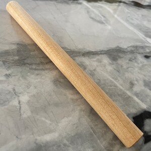 May include: A plain wooden rolling pin, approximately 12 inches long, with a smooth, light brown finish.