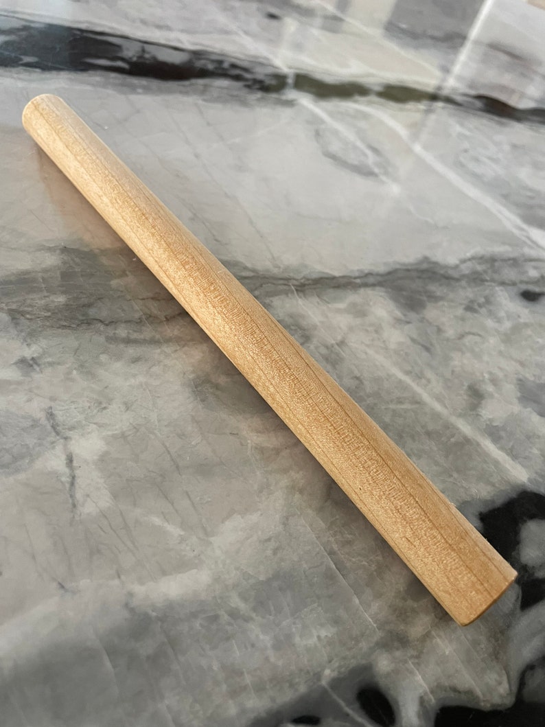 May include: A plain wooden rolling pin, approximately 12 inches long, with a smooth, light brown finish.