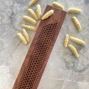 May include: A wooden incense holder with a geometric pattern and a pile of white incense sticks.