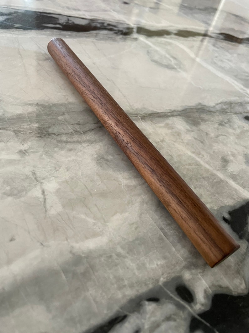 May include: A long, dark brown wooden rolling pin.