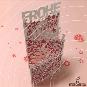May include: A vertical greeting card featuring intricate laser-cut patterns of snowflakes and stars in white and red. The text FROHE WEIHNACHTEN is cut out from the top and middle sections. Small red star and snowflake confetti surround the card.