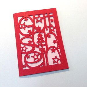 May include: A red card with a white background showing a Christmas-themed design cut out of the card. The design includes stars, ornaments, and a Christmas tree.