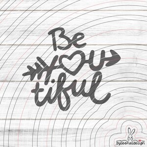 Könnte beinhalten: Graue Grafik mit den handgeschriebenen Worten „Be You tiful“, wobei das Wort „you“ durch ein Herz und einen Pfeil dargestellt wird. Das Design befindet sich auf einem weißen Holzmaserungshintergrund mit konzentrischen Halbkreisen.