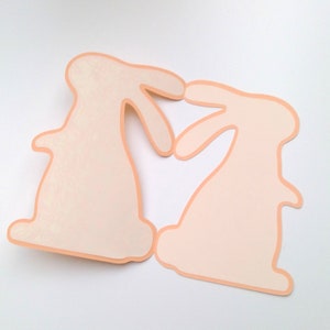 May include: Two peach-colored paper bunny cutouts facing each other, forming a heart shape.