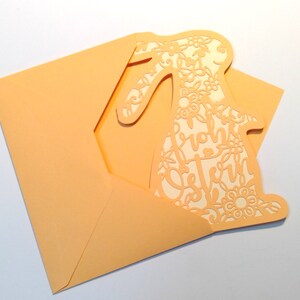 May include: A peach-colored card with a cutout of a bunny rabbit. The bunny is decorated with floral designs and the text "Frohe Ostern" is written inside the bunny.