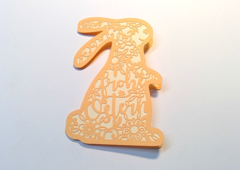 May include: A peach-colored paper Easter bunny card with a floral design and the text "Frohe Ostern" in white.