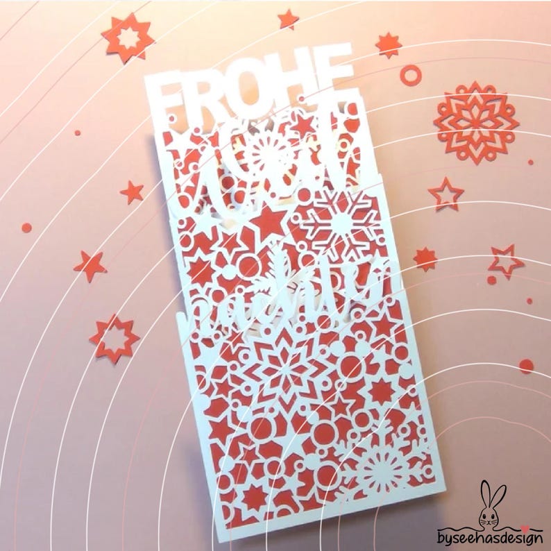 May include: A rectangular white paper cutout card featuring intricate laser-cut patterns of snowflakes, stars, and circles. The text FROHE WEIHNACHTEN is cut out in a bold, stylized font. The card is layered over a solid red background.