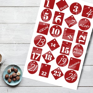 Könnte beinhalten: Rote und weiße Weihnachts-Adventskalender-Aufkleber mit den Zahlen 1 bis 24. Die Aufkleber haben verschiedene Formen, darunter Kreise, Quadrate und Rauten.