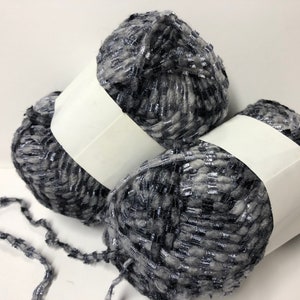 May include: Three balls of gray and silver yarn with white labels. The yarn has a fuzzy texture.