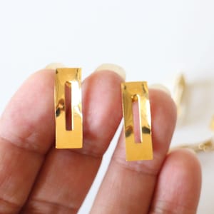 Puede incluir: Dos pinzas para el pelo de metal de color dorado, de forma rectangular con una abertura estrecha en el centro.
