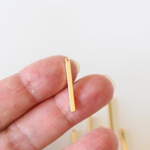 Peut inclure: Pendentif en forme de barre dorée avec une boucle en haut. Le pendentif mesure environ 2,5 cm de long.