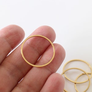 Pode incluir: Um conjunto de cinco argolas de metal douradas, cada uma com uma forma circular lisa. As argolas estão dispostas em uma pilha, com a maior argola na parte inferior e a menor argola na parte superior.
