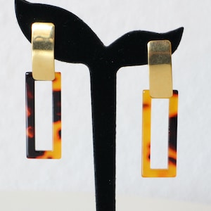 Puede incluir: Un par de pendientes rectangulares de oro y carey. Los pendientes tienen una barra de oro en la parte superior y un rectángulo de carey con un contorno de oro que cuelga.