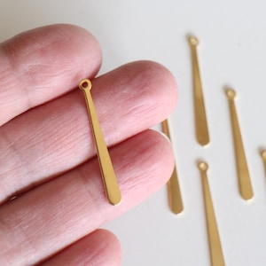 Pode incluir: Pingentes de metal dourado com forma oval pontiaguda e um pequeno laço na parte superior. Os pingentes medem aproximadamente 3,8 cm de comprimento.