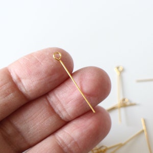 May include: Gold-coloured head pins with a loop at one end. The pins are approximately 2.5 cm long.