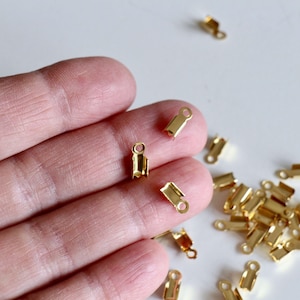 Op de afbeelding: Een close-up van een stapel gouden metalen sluitingen. De sluitingen zijn klein en hebben een eenvoudig ontwerp. Ze zijn perfect om een ​​toets van elegantie toe te voegen aan sieraden of andere knutselprojecten.