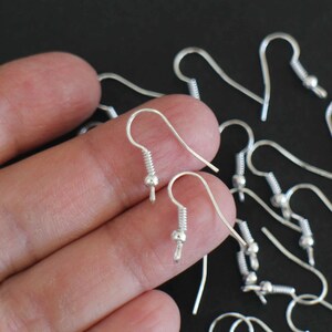 May include: Silver earring hooks with a small ball at the end. The hooks are made of metal and are designed to be used with earrings.