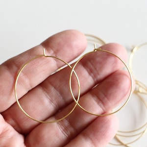 Peut inclure: Deux créoles dorées, l'une sur l'autre, tenues dans une main. Les créoles sont simples et circulaires.