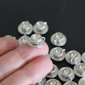 Peut inclure: Une collection de tasses à thé et de soucoupes miniatures en argent. Les tasses et les soucoupes sont détaillées avec un motif en relief et ont une finition brillante.