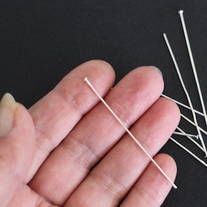 Peut inclure: Gros plan sur une main tenant un groupe d'épingles à tête argentées. Les épingles mesurent environ 5 cm de long et ont une tête arrondie.