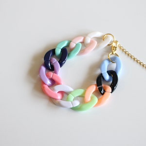 Könnte beinhalten: Ein farbenfrohes, dickes Kettenarmband mit einem goldenen Verschluss und einer Verlängerungskette. Das Armband ist aus Kunststoff und in verschiedenen Pastellfarben gehalten, darunter Rosa, Blau, Grün und Weiß.