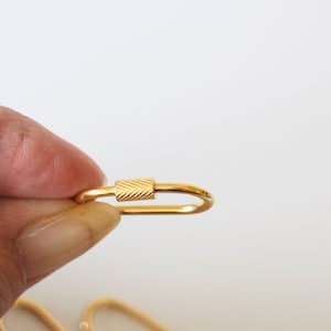 May include: A gold-colored metal key chain with a textured oval ring and a small, textured, rectangular clasp.