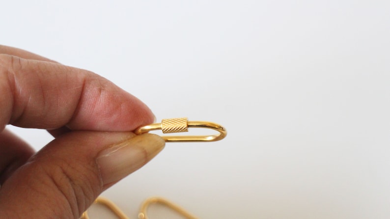 May include: A gold-colored metal key chain with a textured oval ring and a small, textured, rectangular clasp.