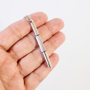 Op de afbeelding: Een zilverkleurige hangerketting met een kleine schroevendraaierbedel. De bedel heeft een geribbelde handgreep en een punt. De ketting wordt getoond tegen een effen witte achtergrond.