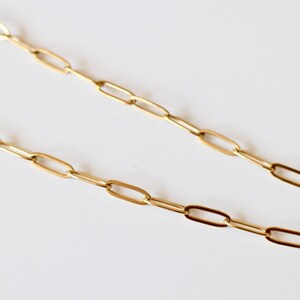 Puede incluir: Un collar de cadena en tono dorado con eslabones rectangulares alargados. La cadena est&aacute; compuesta por una serie de eslabones met&aacute;licos pulidos y uniformes conectados en un patr&oacute;n continuo y repetitivo, creando un dise&ntilde;o de joyer&iacute;a simple.