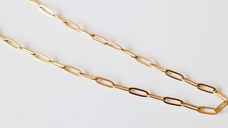 Puede incluir: Un collar de cadena en tono dorado con eslabones rectangulares alargados. La cadena est&aacute; compuesta por una serie de eslabones met&aacute;licos pulidos y uniformes conectados en un patr&oacute;n continuo y repetitivo, creando un dise&ntilde;o de joyer&iacute;a simple.