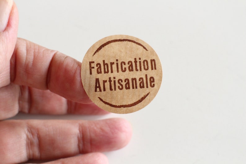 May include: A brown paper circle sticker with the text "Fabrication Artisanale" in brown lettering.
