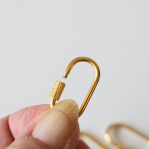 May include: A gold-colored metal key chain with a swivel clasp. The clasp is open and the key chain is held in a hand.
