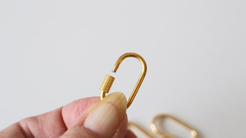 May include: A gold-colored metal key chain with a swivel clasp. The clasp is open and the key chain is held in a hand.